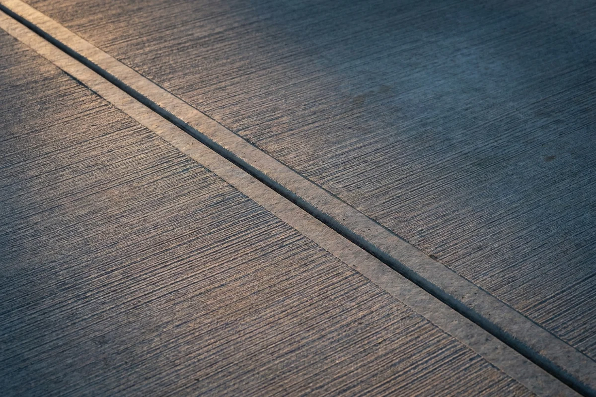 Close-up detail of a broom-finish concrete surface with a crisp sawcut control joint running diagonally across the frame